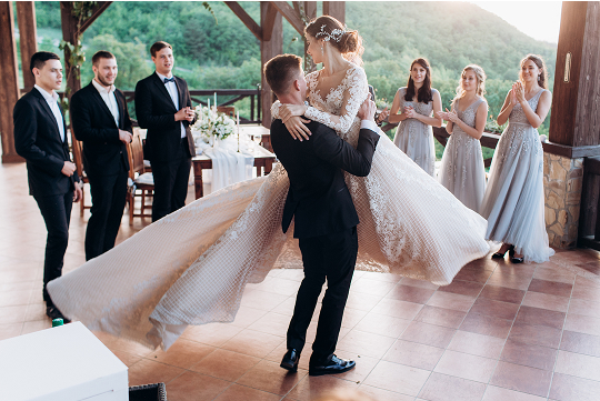 A bride and groom share a romantic dance during their wedding reception, surrounded by joyful guests and elegant decorations.