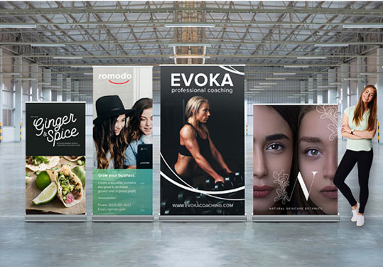 A woman stands beside three roll-up banners, showcasing various designs and information in a professional setting.