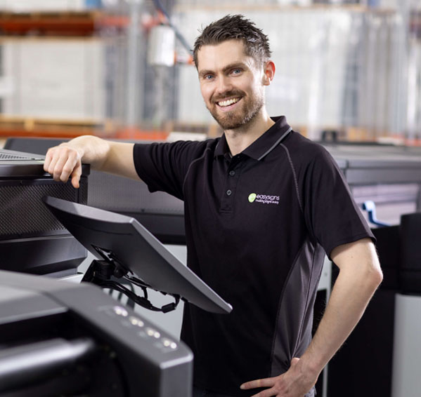 A man stands in front of a large printer, observing its operation with a focused expression.
