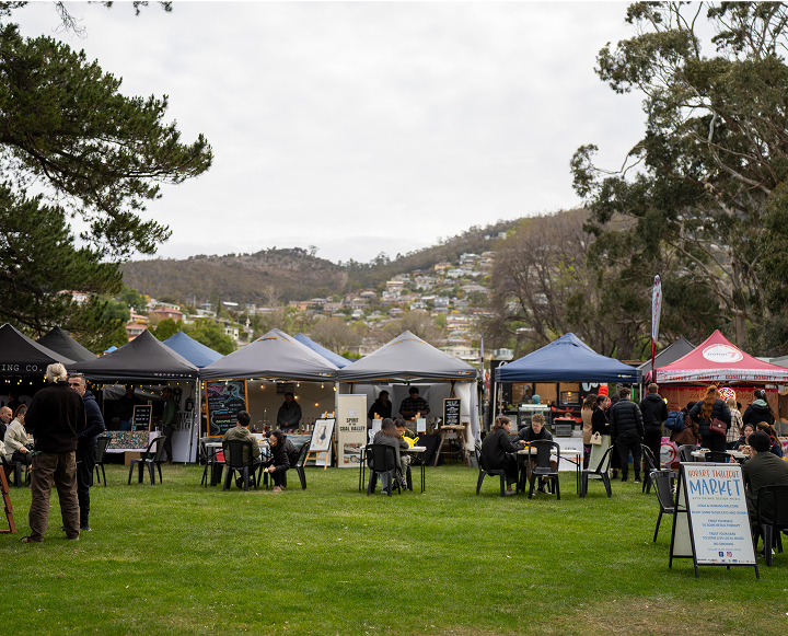 A group of people seated under blue tents, engaged in conversation and enjoying the outdoor setting.