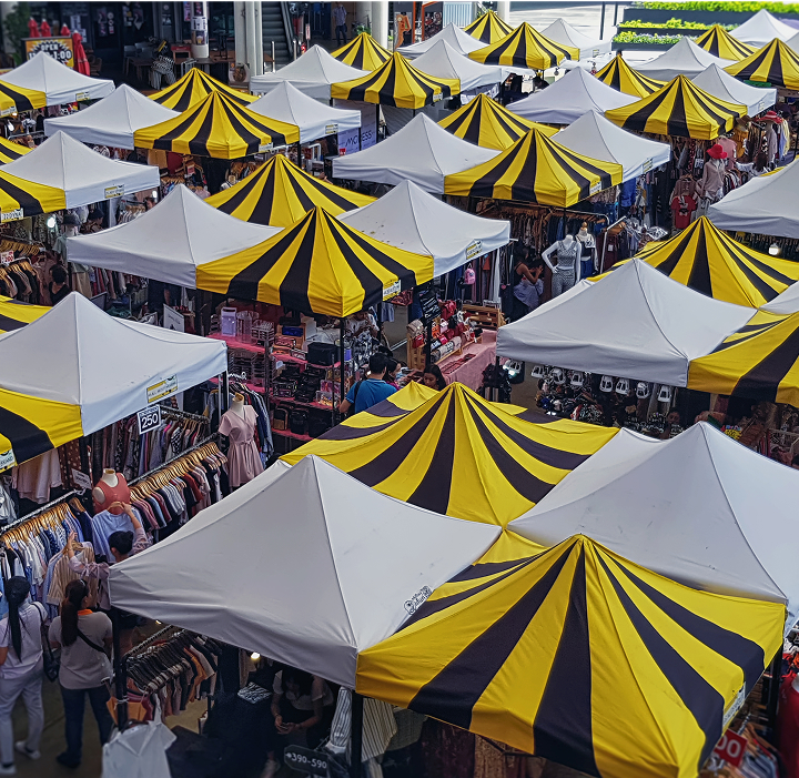 A bustling outdoor market featuring numerous colorful tents and a diverse crowd of shoppers exploring various stalls.