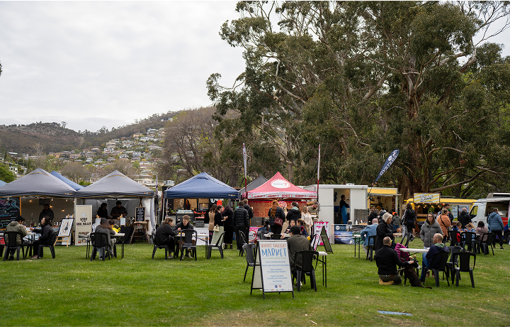 A group of people seated at tables on a grassy area, enjoying a gathering in an outdoor setting.