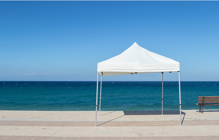 A white tent on a sandy beach, accompanied by a wooden bench nearby, with gentle waves in the background.