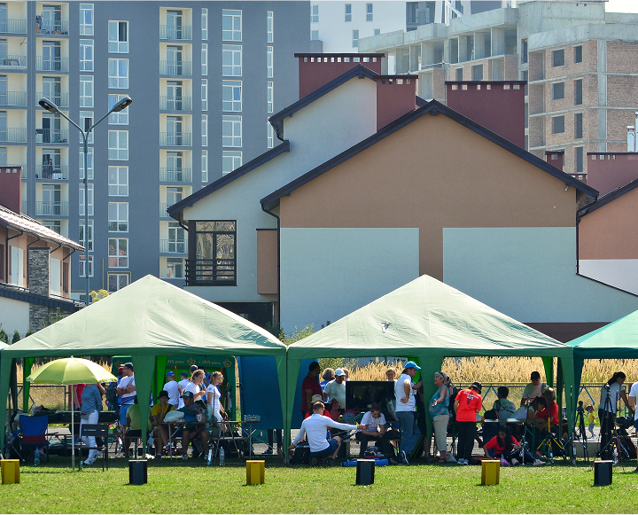 A diverse group of people seated together under a large green tent, engaged in conversation and enjoying their time.