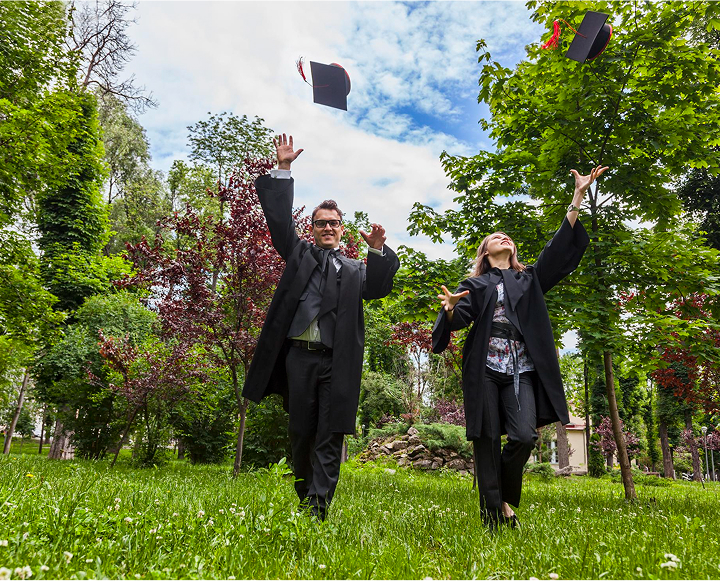 Two graduates in gowns joyfully throw their caps into the air, celebrating their achievement on graduation day.