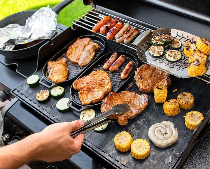 A person grilling food on a stovetop with a grill pan, surrounded by various ingredients and kitchen utensils.