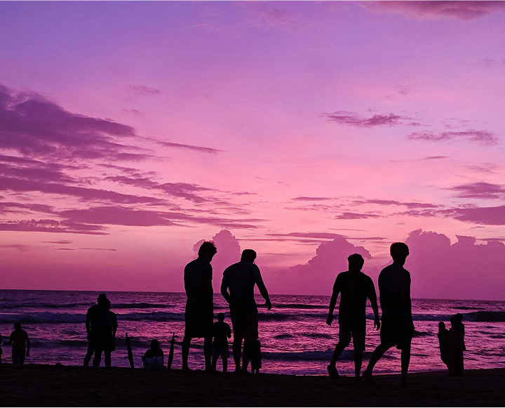 A diverse group of people enjoying a sunny day on the beach, some sitting on towels and others playing in the sand.