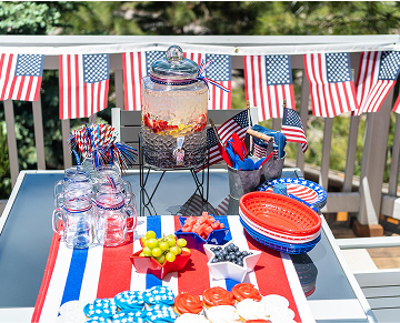 Patriotic party setup for the 4th of July featuring red, white, and blue decorations, table settings, and festive snacks.